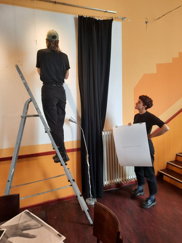 Zwei junge Frauen hängen Bilder an die Wände auf. Eine steht auf einer Leiter.