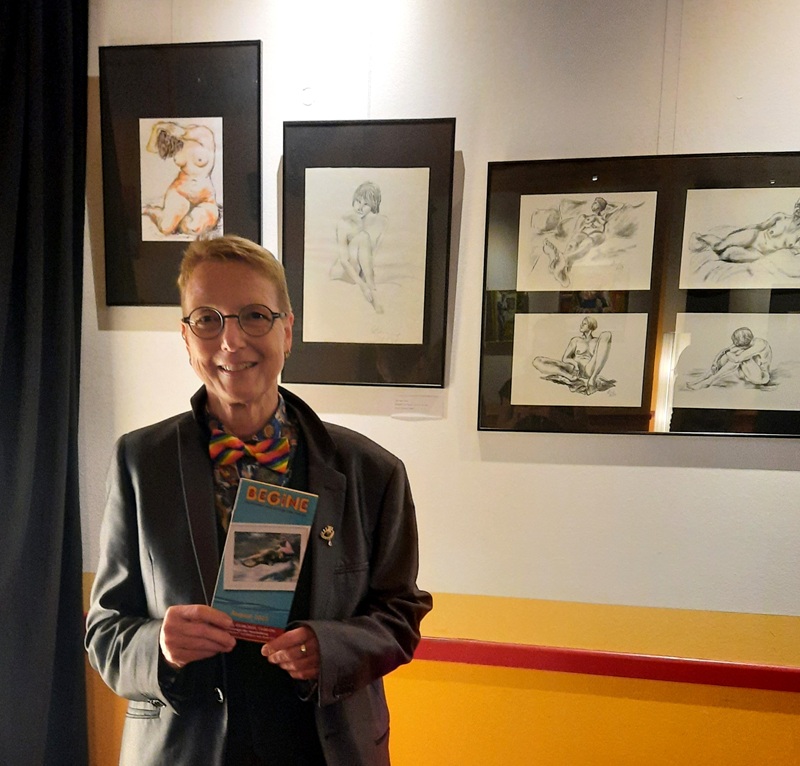 Ein Foto von einer Frau mit kurzem Haar und Brille, die das Begine-Programm in einer Hand hält und lächelt uns an! 