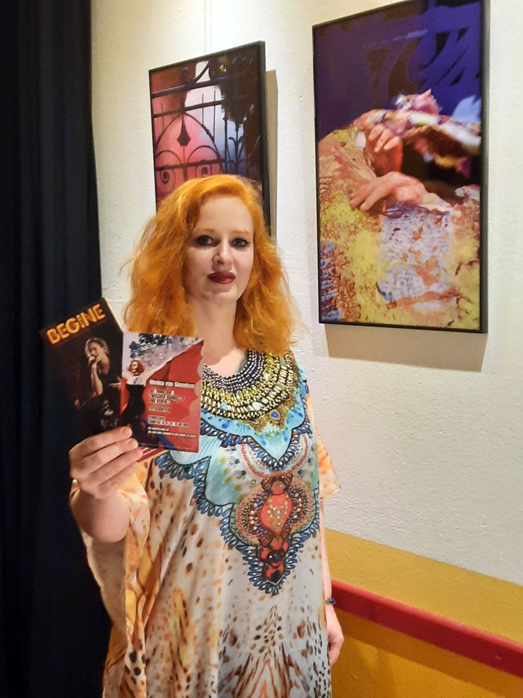 Ein Foto von einer Frau mit rotem Haar in einem bunten Kleid, die ein Begine-Programm in einer Händ hällt. 